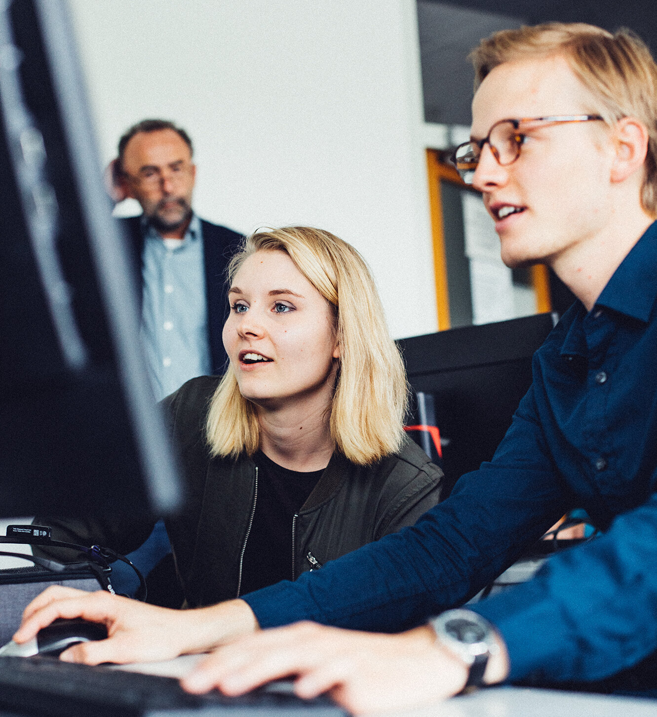 student using a computer, a fellow student and a tutor look on student using a computer, a fellow student and a tutor look on